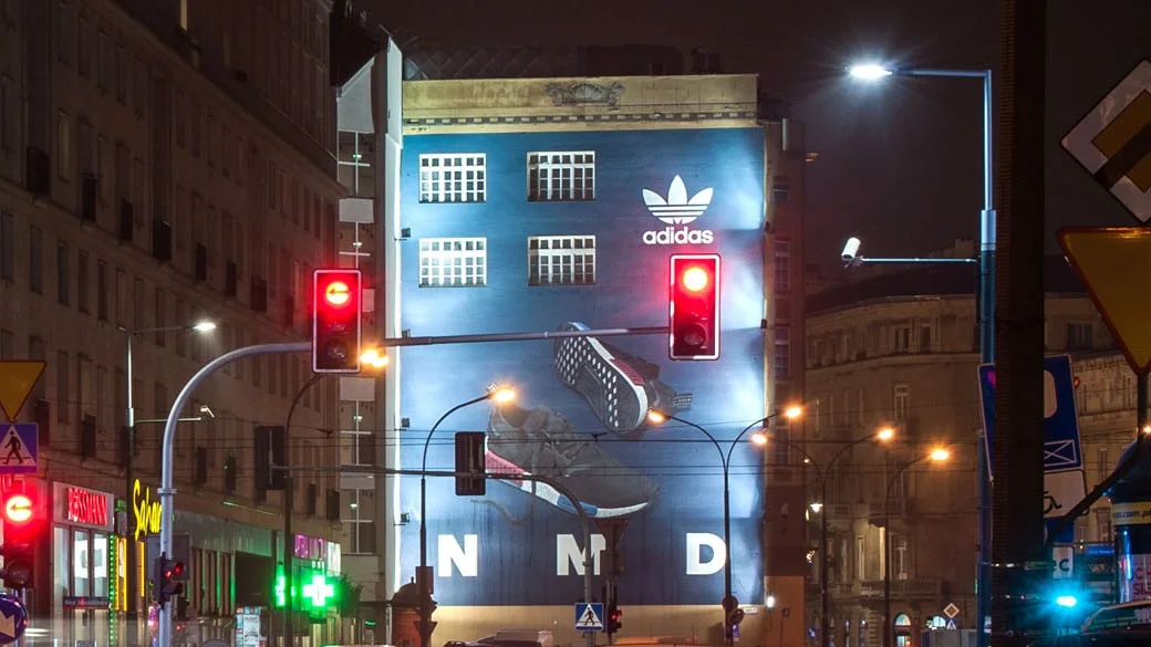 Podświetlony nocą mural adidas NMD nad ruchliwą ulicą w Warszawie